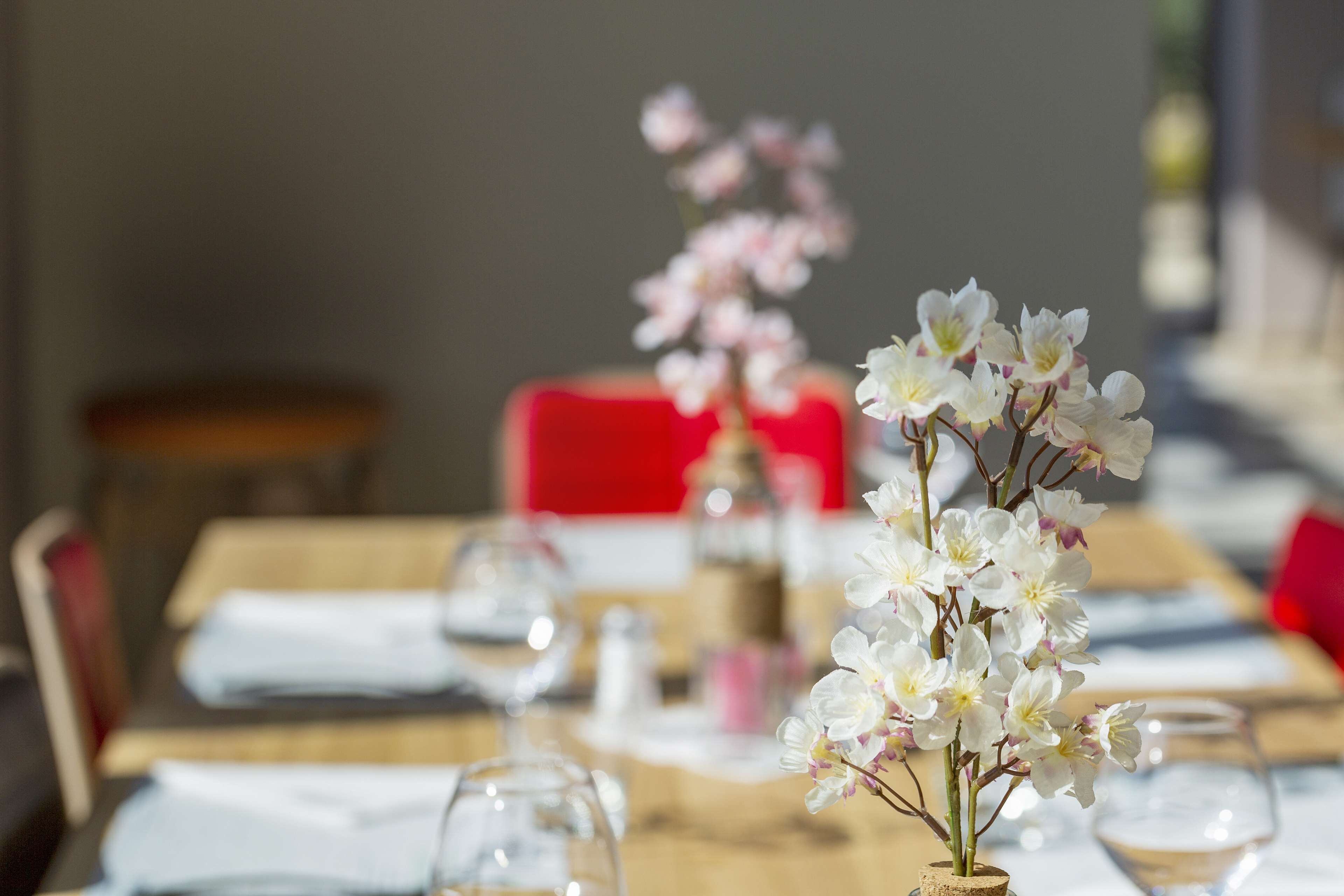 A dining table with white tablecloths, clear glass wine glasses, and a vase with white flowers.