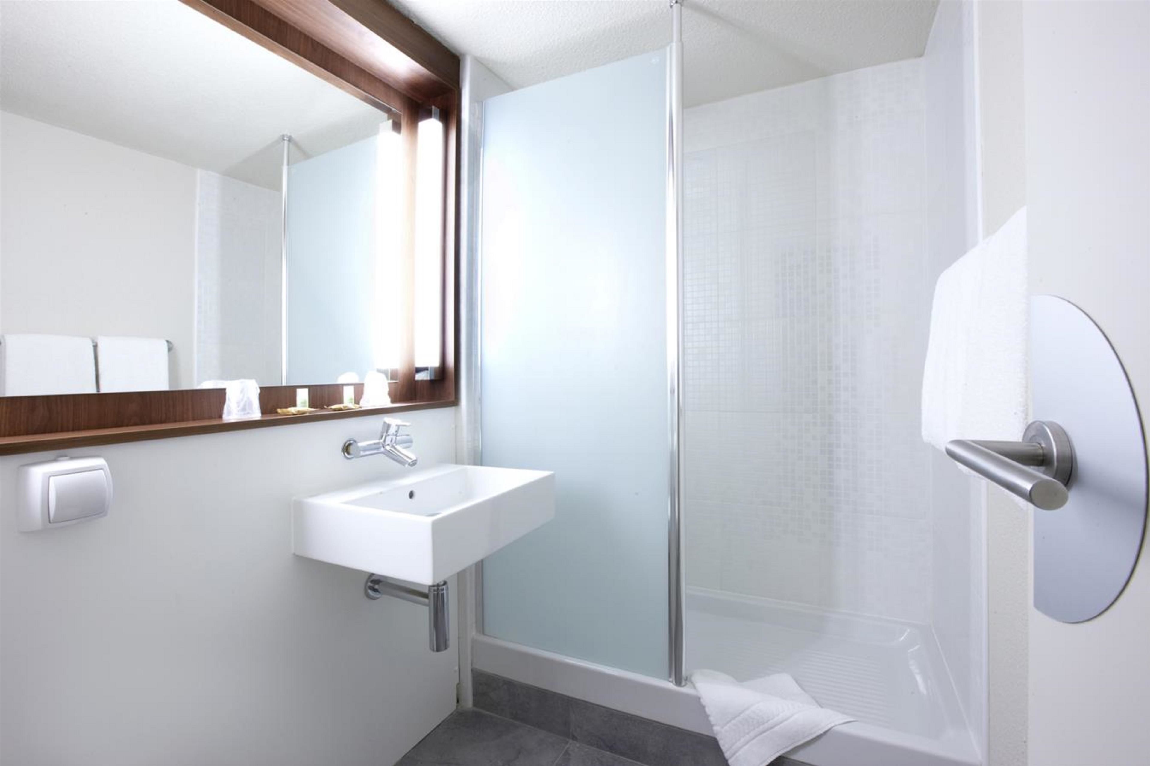 A modern bathroom with a glass shower enclosure, a white sink, and a mirror with a wooden frame.