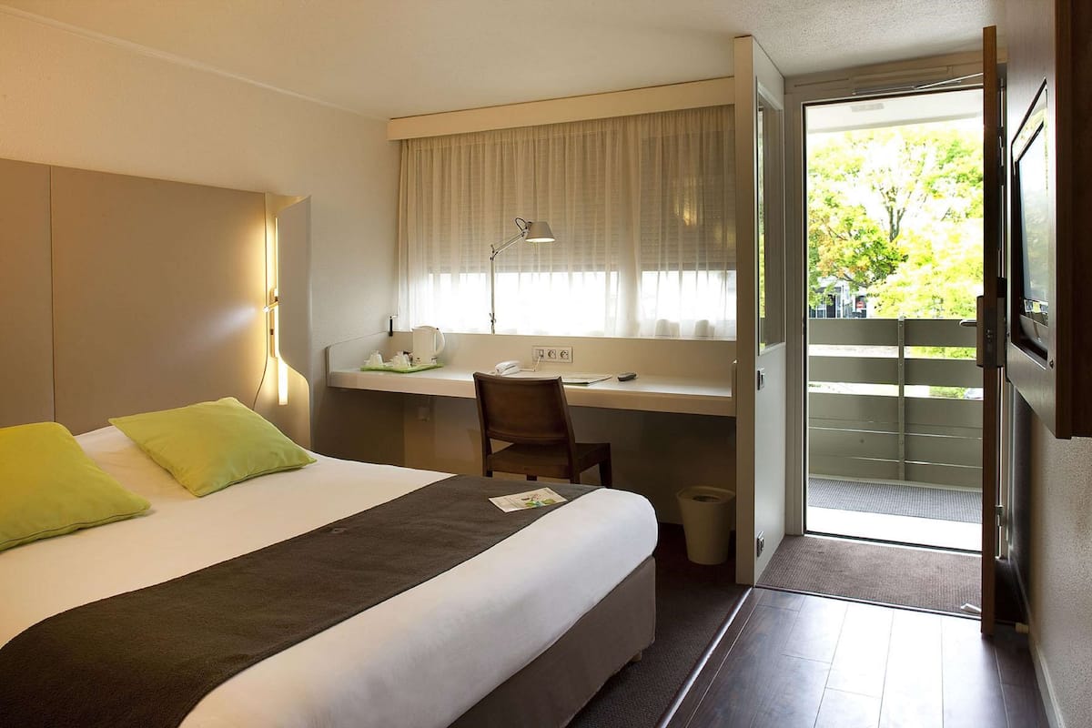 Habitación de hotel con cama, escritorio, silla y vistas al exterior.