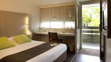 A hotel room with a bed, desk, chair, and a view of the outdoors.