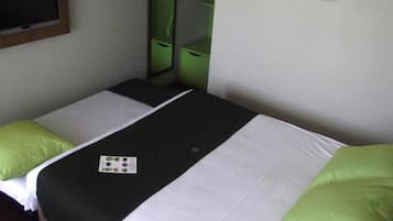 Una habitación pequeña con una cama individual, una colcha verde y blanca, una mesita con un mantel individual y un espejo en la pared.
