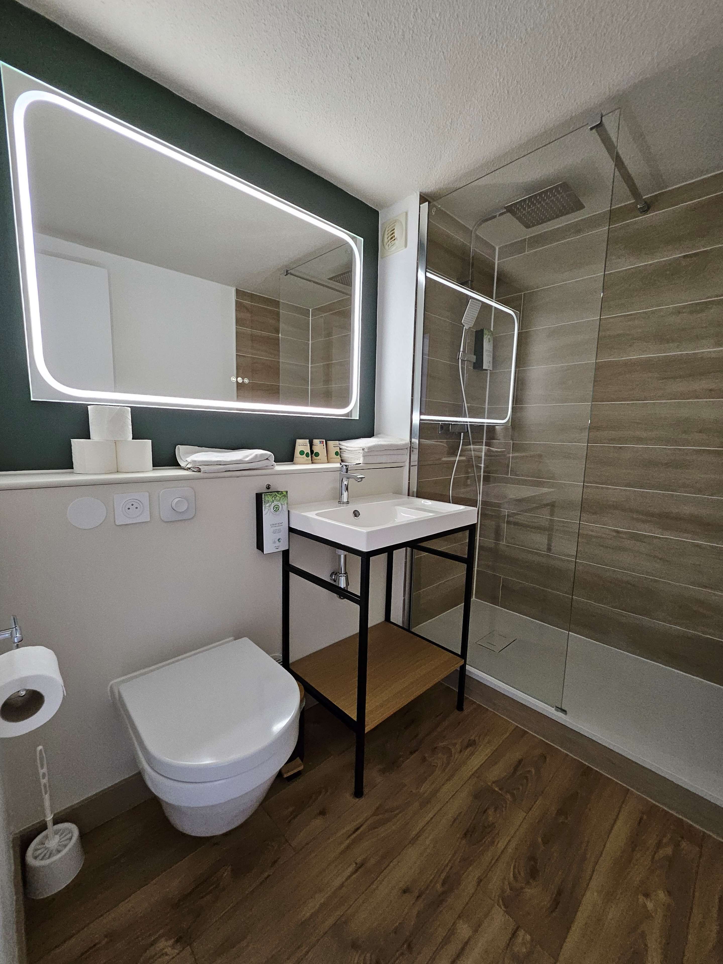 Une salle de bain moderne avec un lavabo blanc, un grand miroir, des toilettes et une douche à parois de verre.
