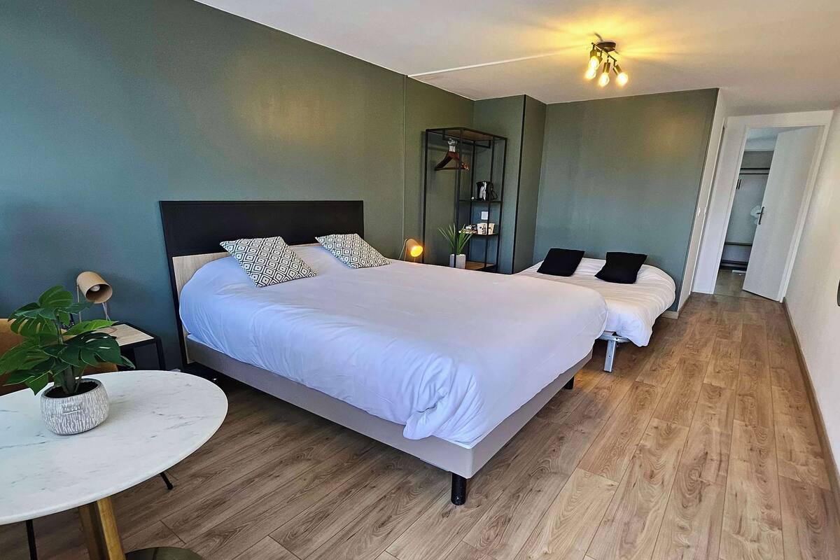 Una habitación de hotel moderna con dos camas, una mesita redonda pequeña y una planta en maceta.