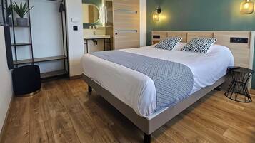 A modern bedroom with a large bed, a wooden floor, a bathroom with a mirror and sink, and a green accent wall.