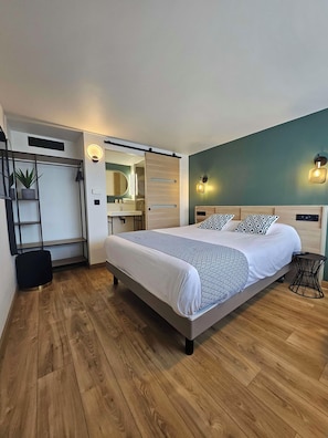 A modern bedroom with a large bed, a wooden floor, a bathroom with a mirror and sink, and a green accent wall. - Campanile Chartres (Chartres)