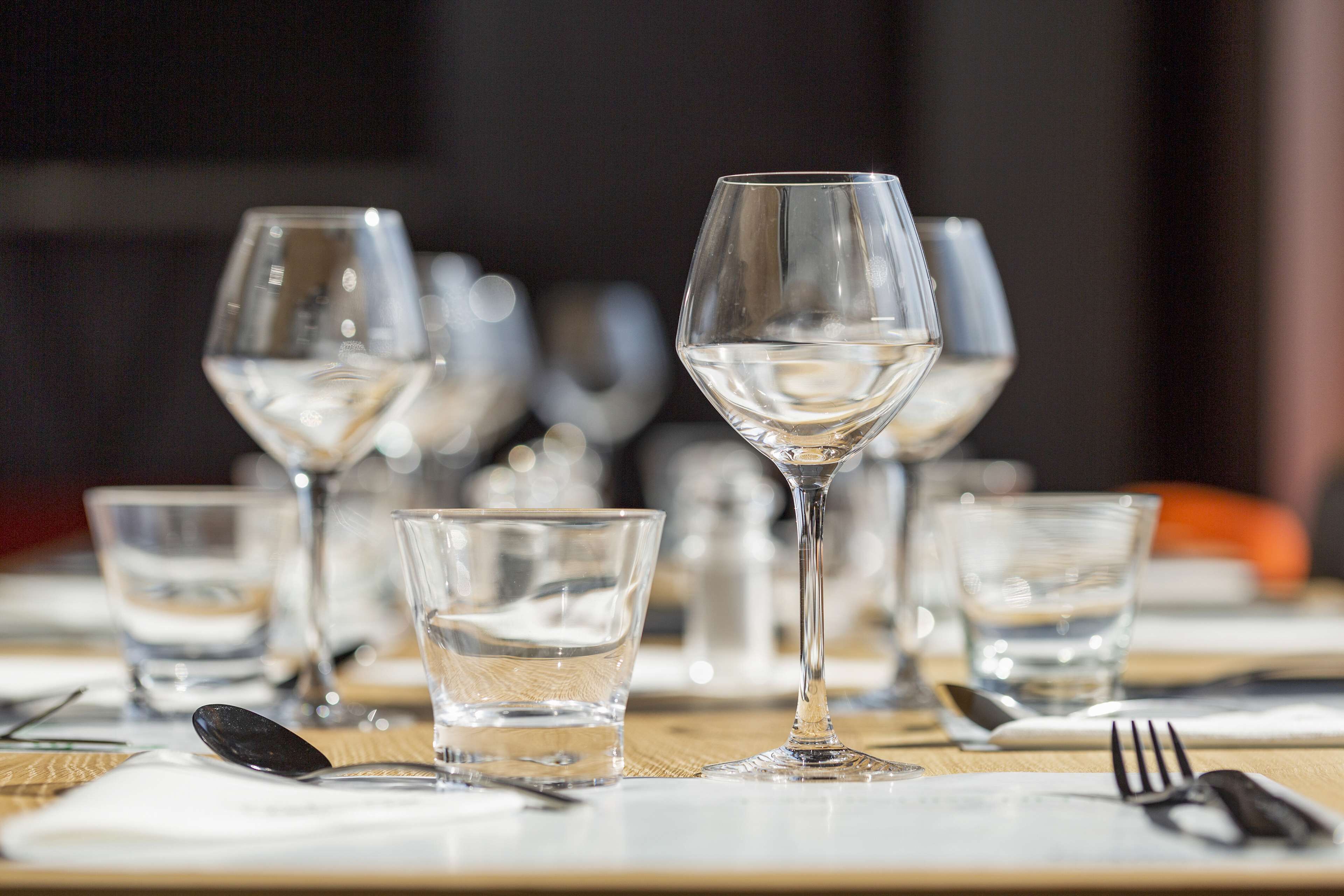 A dining table set with multiple wine glasses and water glasses, utensils, and a napkin.