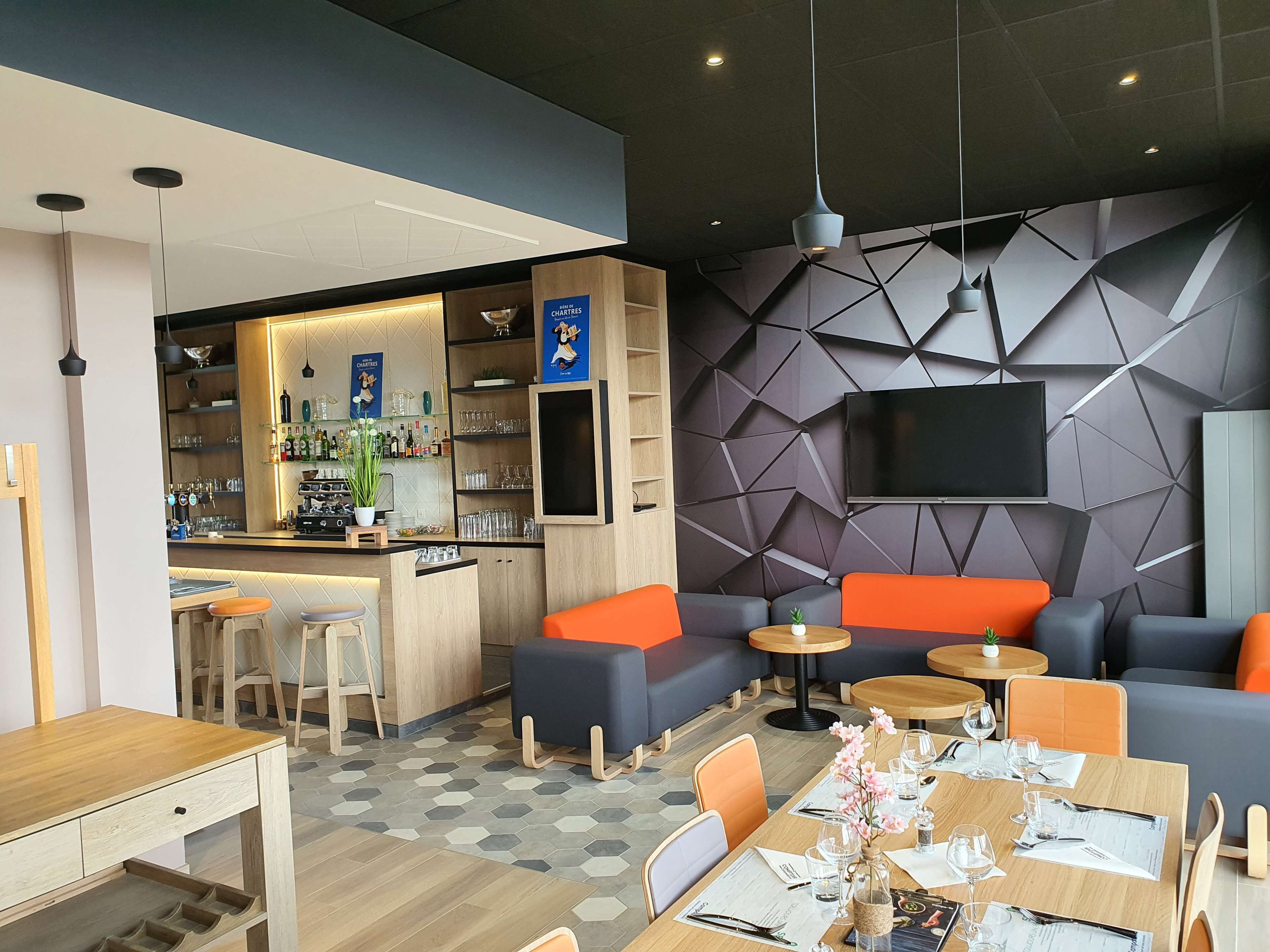 Un moderno bar con mostrador, taburetes, y una gran variedad de botellas y copas. Hay una zona de estar con sofás y mesas, y un televisor montado en la pared.