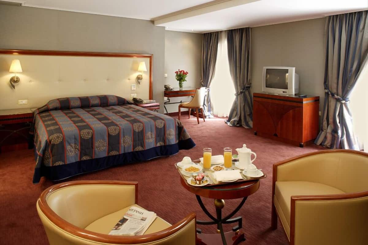 Une chambre d’hôtel comprenant un lit, un bureau avec une chaise, une télévision et une table à manger avec des articles pour le petit-déjeuner.