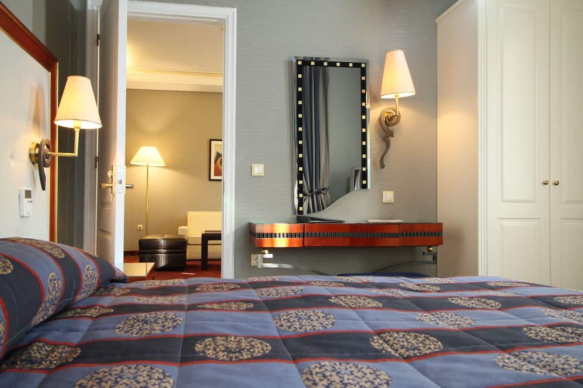 Une chambre d’hôtel avec un lit, une coiffeuse avec un miroir, une lampe et une porte donnant sur une autre pièce.