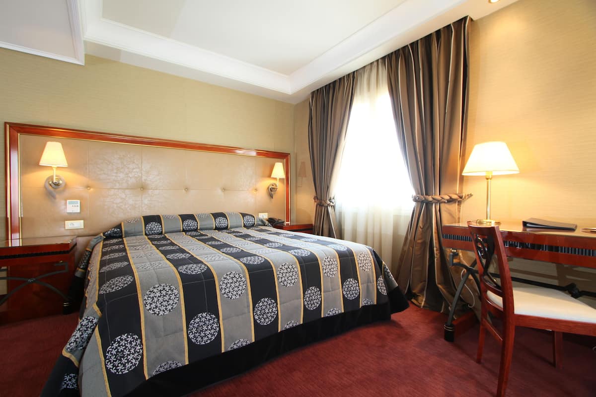 Une chambre d’hôtel avec un grand lit, un bureau, une chaise et deux lampes.