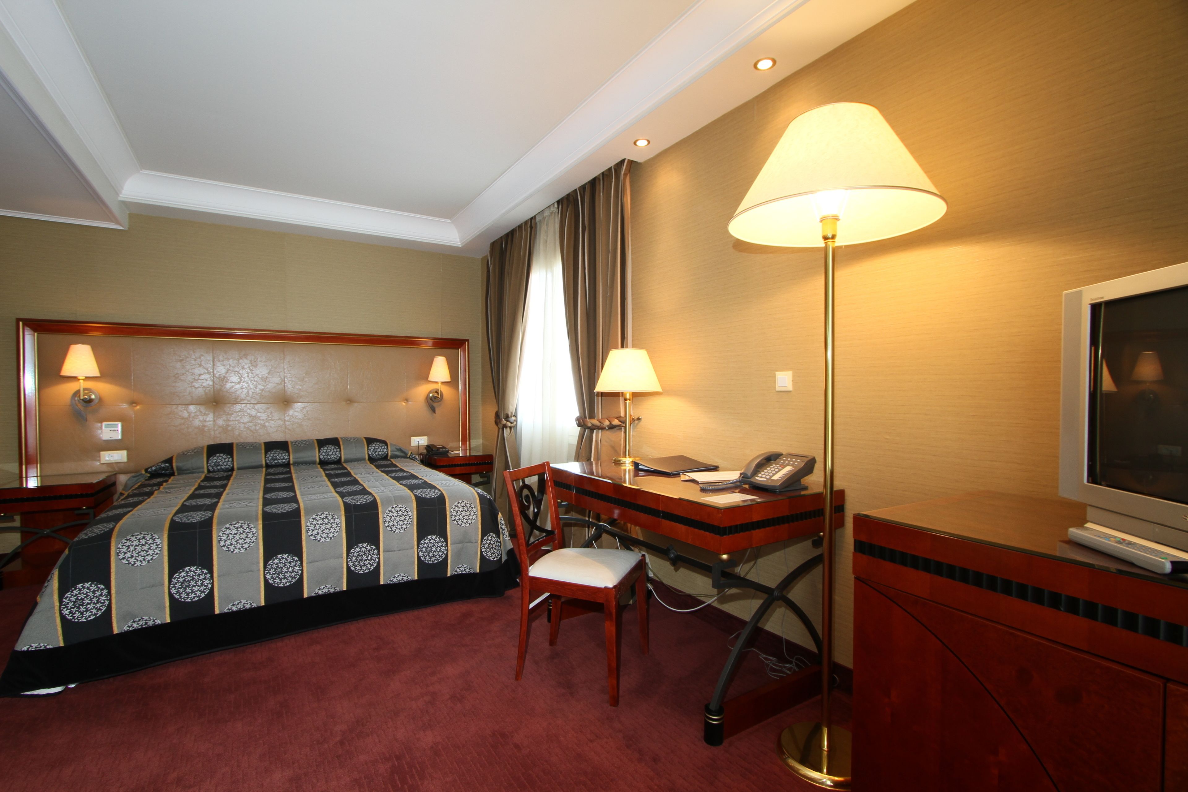 Una habitación de hotel con una cama grande, un escritorio con lámpara, una silla y un televisor.