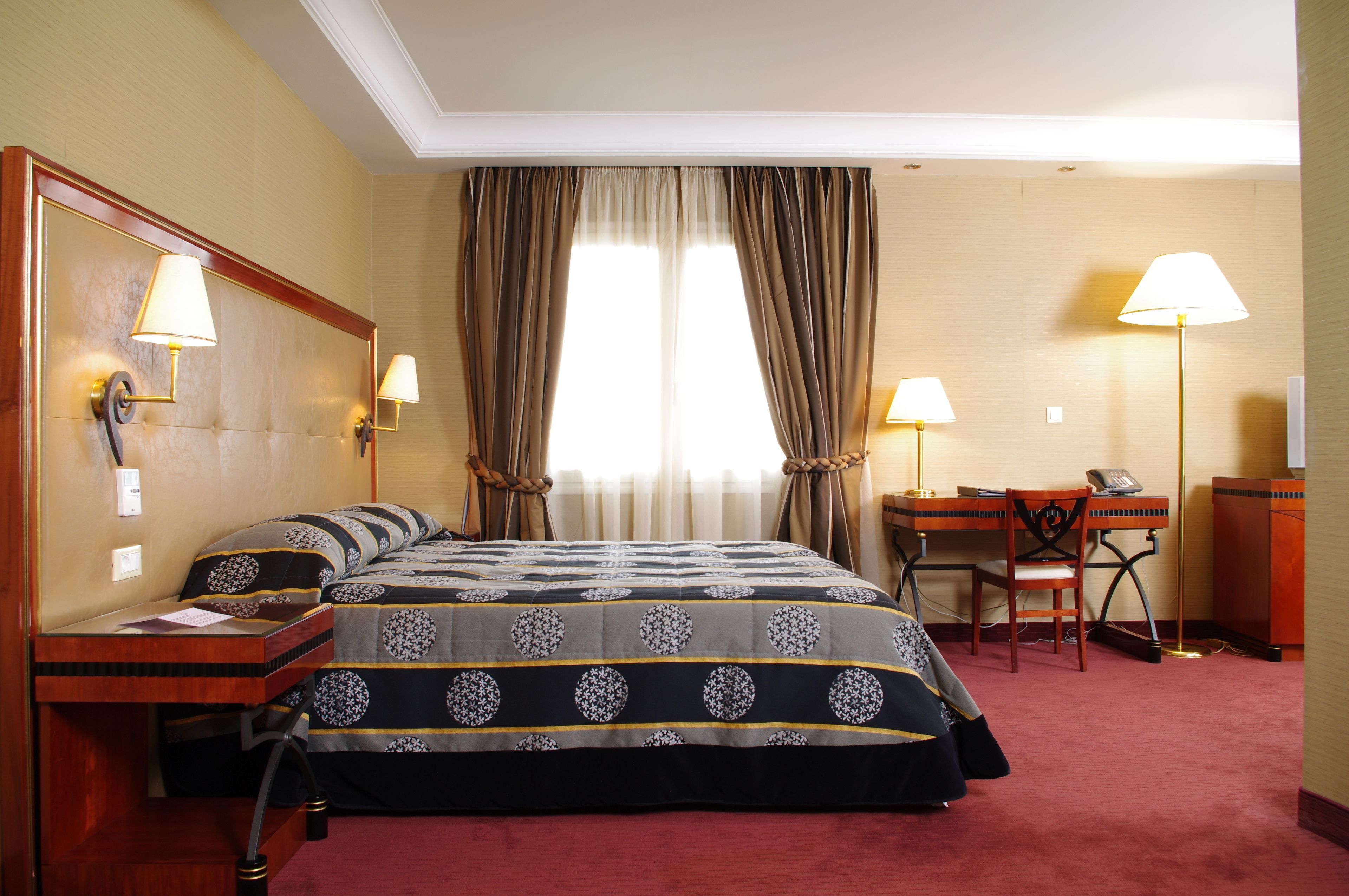 A hotel room with a bed, a desk, two lamps, and a chair.