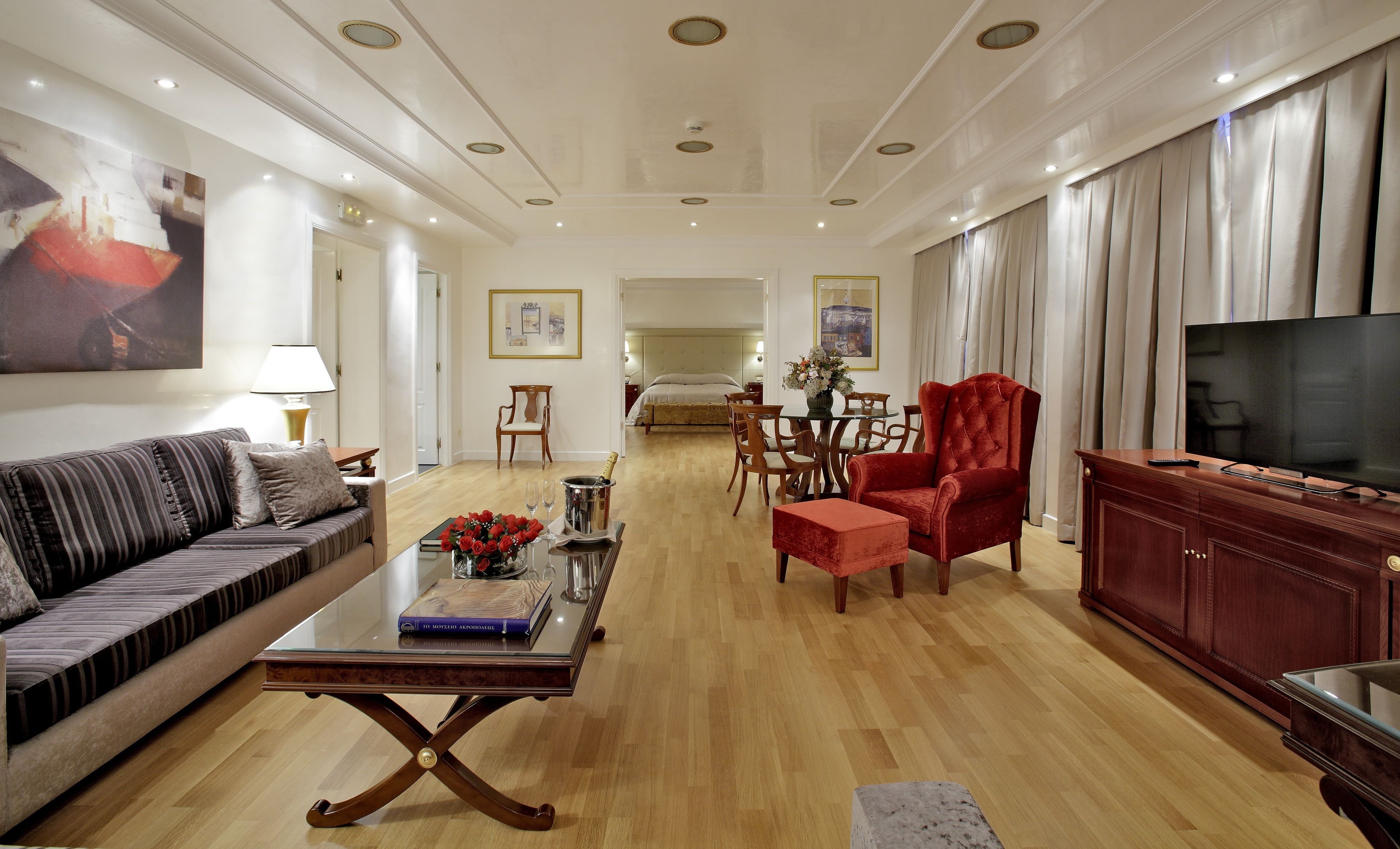A spacious living room with a sofa, a red armchair, a coffee table, and a TV.