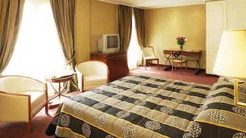 Una habitación de hotel con una cama grande, un escritorio con televisor, una silla y una lámpara.
