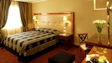 Ein Hotelzimmer mit einem großen Bett, einem Nachttisch mit Lampe, einem kleinen Tisch mit einer Fruchtschale und einem Stuhl.