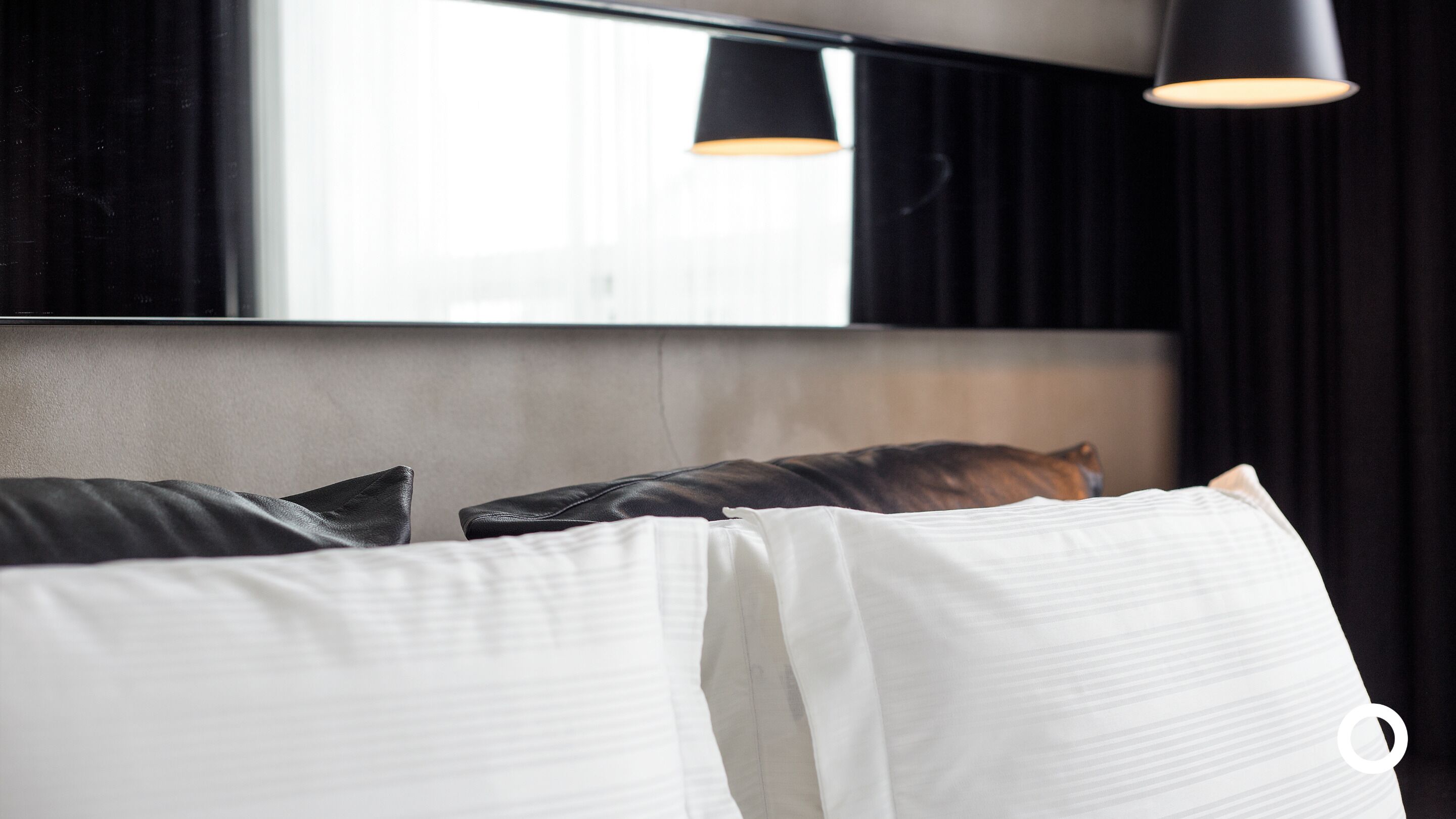 Een hotelkamer met een bed, kussens, een hoofdbord en een hanglamp.