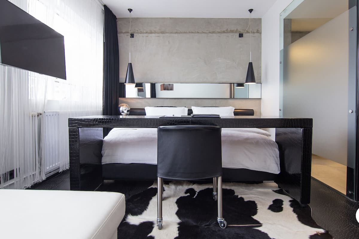 A modern bedroom with a large bed, a small seating area, and a bathroom visible through an open door.