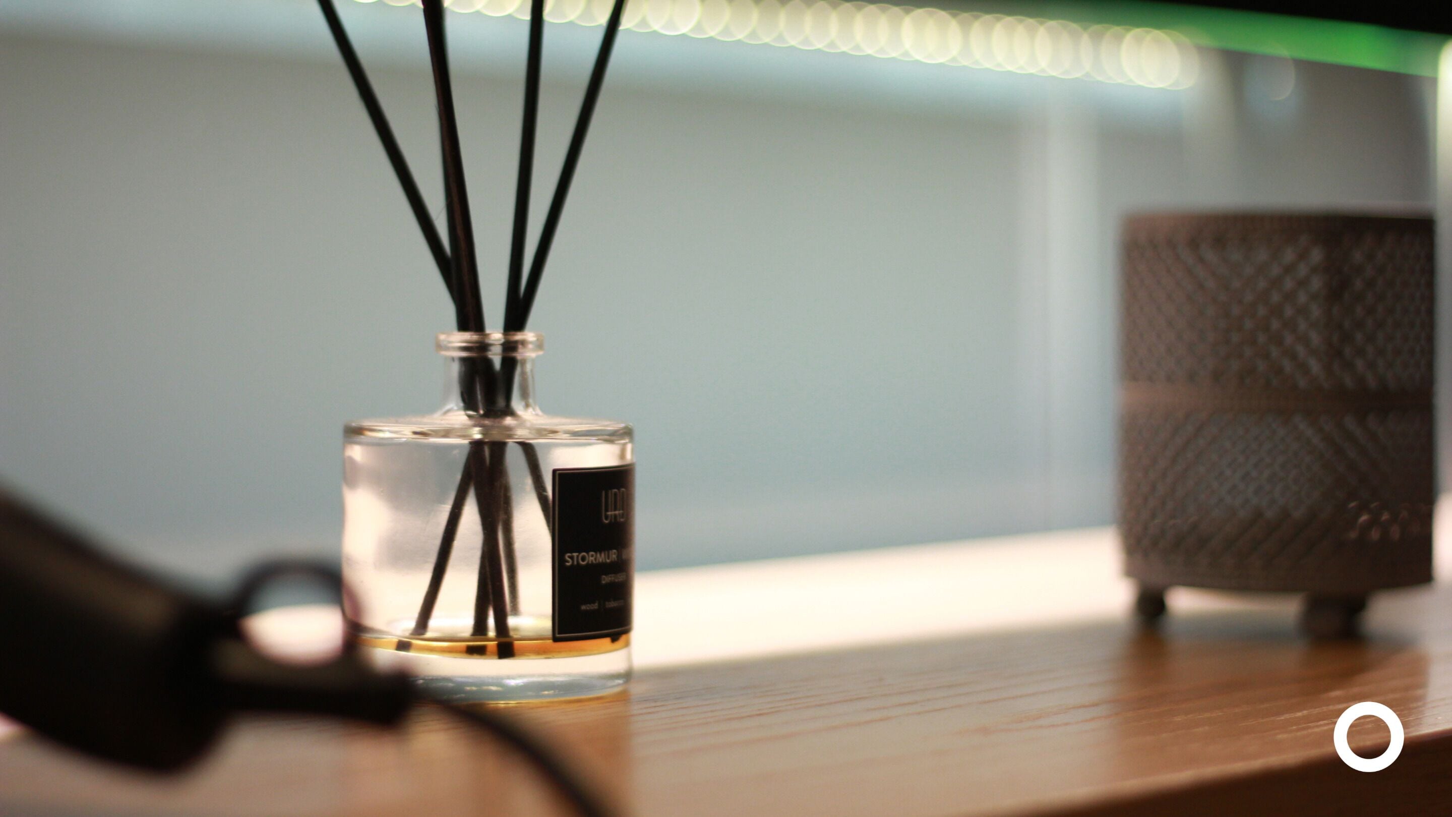 Une bouteille en verre transparent avec des étiquettes noires, posée sur une surface en bois, accompagnée d’un objet noir et d’un récipient texturé.