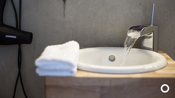 A bathroom sink with running water, a white towel, and a hairdryer on a wooden counter.