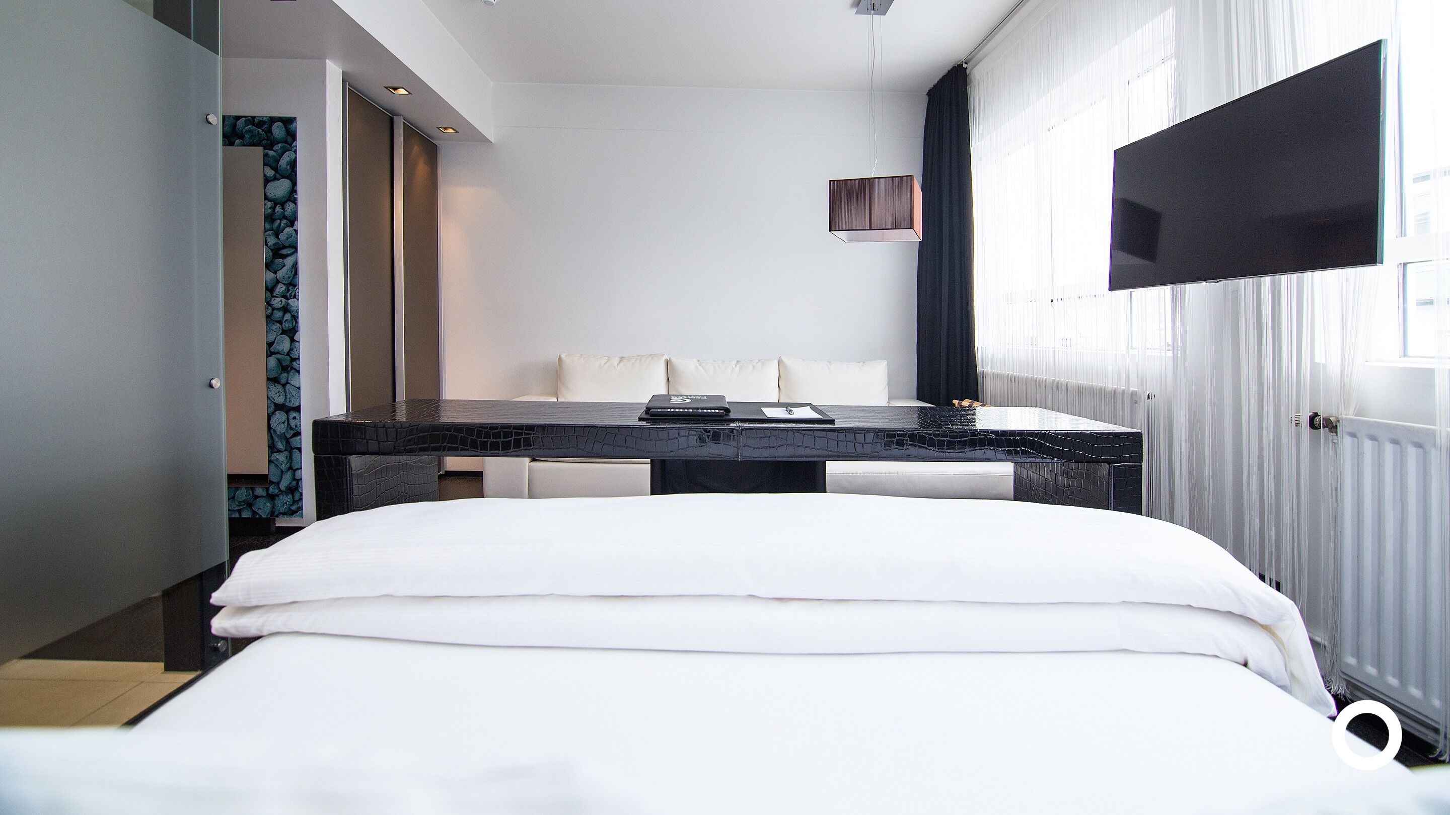 A modern hotel room with a bed, a small table with a laptop, a sofa, and a TV mounted on the wall.