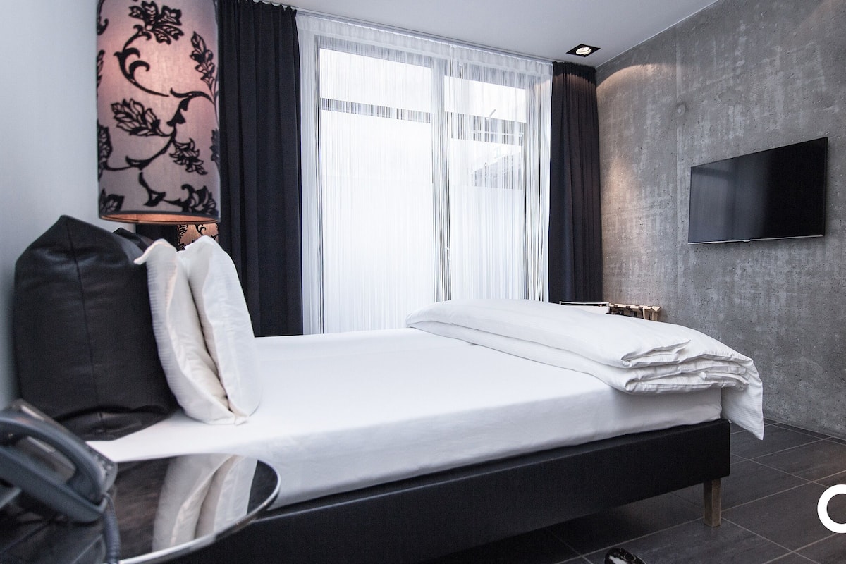 A modern hotel room with a bed, a TV mounted on the wall, and a window with curtains.