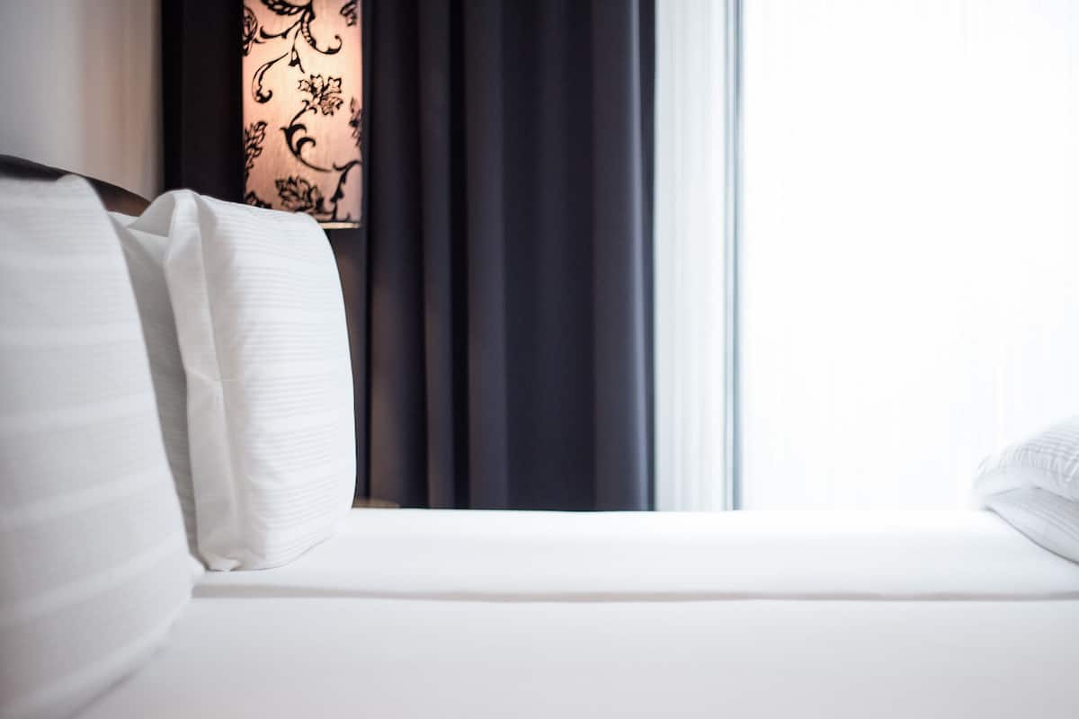 A hotel room with a bed, dark curtains, and a window with a view.