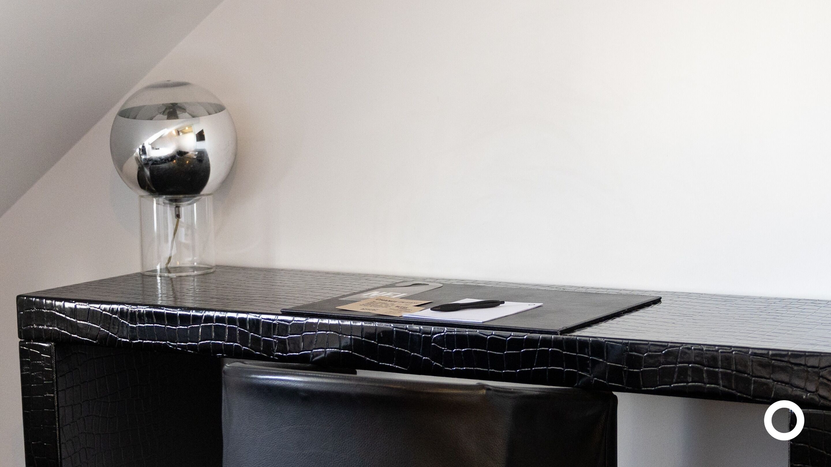A modern, sleek desk with a black marble top, a clear glass vase with a black object inside, and a small white card on the surface.