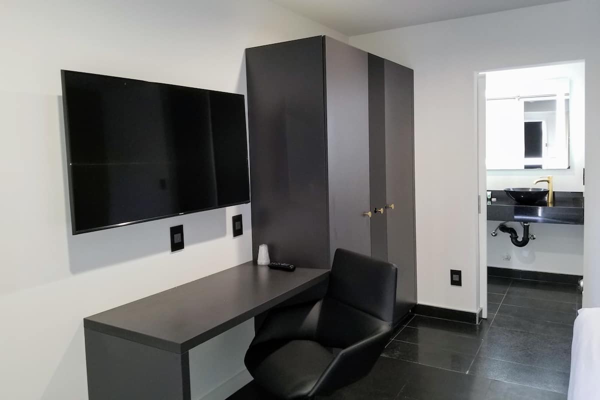 A modern room with a flat-screen TV mounted on the wall, a black chair, and a dark-colored desk.