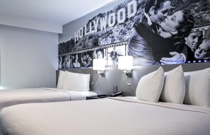 Habitación de hotel con dos camas, un mural de temática de Hollywood y una mesita de noche con una lámpara.