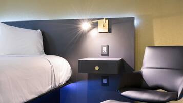 Une chambre d’hôtel comprenant un lit, une table de chevet, une chaise et un luminaire fixé au mur.