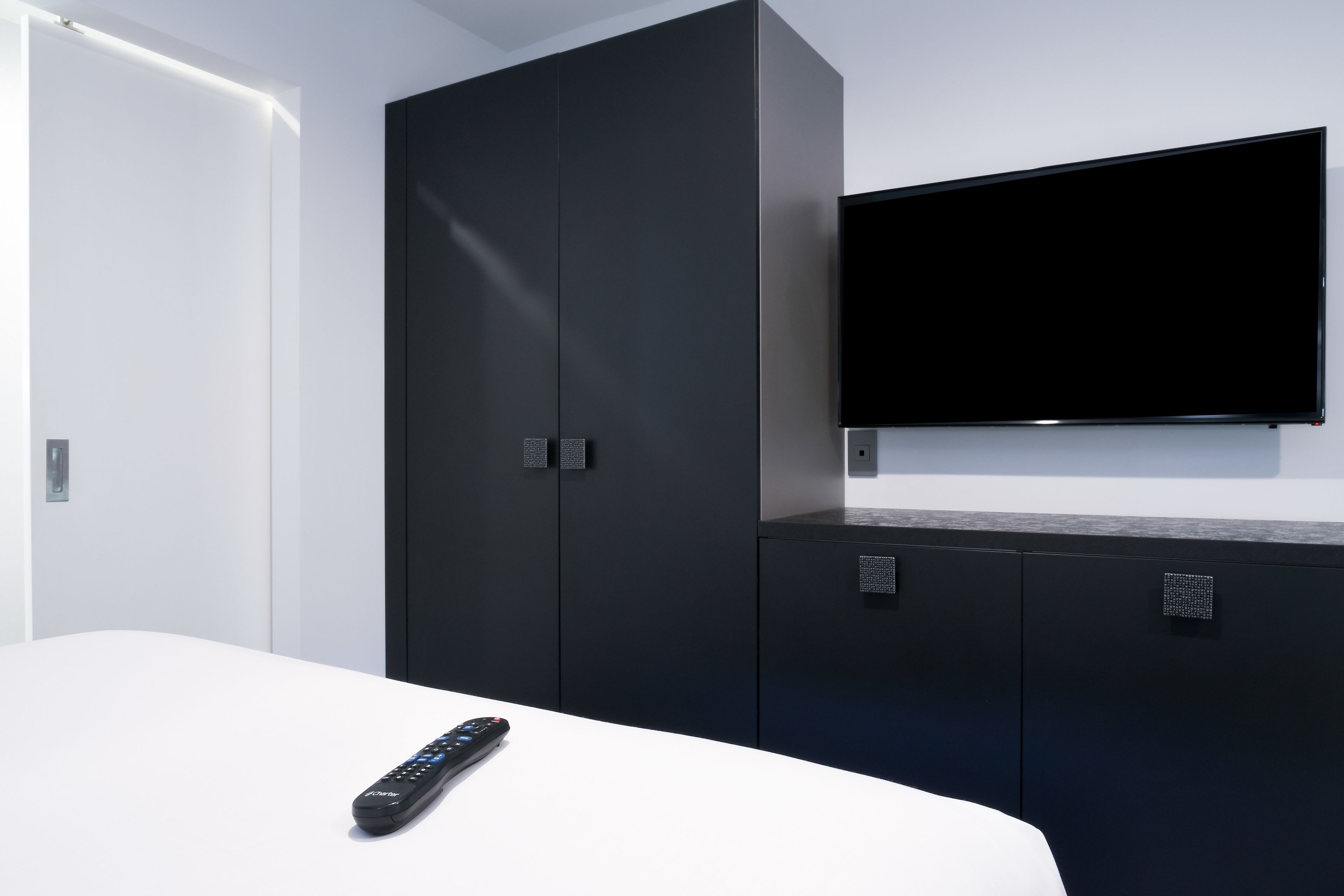 Habitación de hotel moderna con una cama, un televisor montado en la pared y un armario con panel de control.