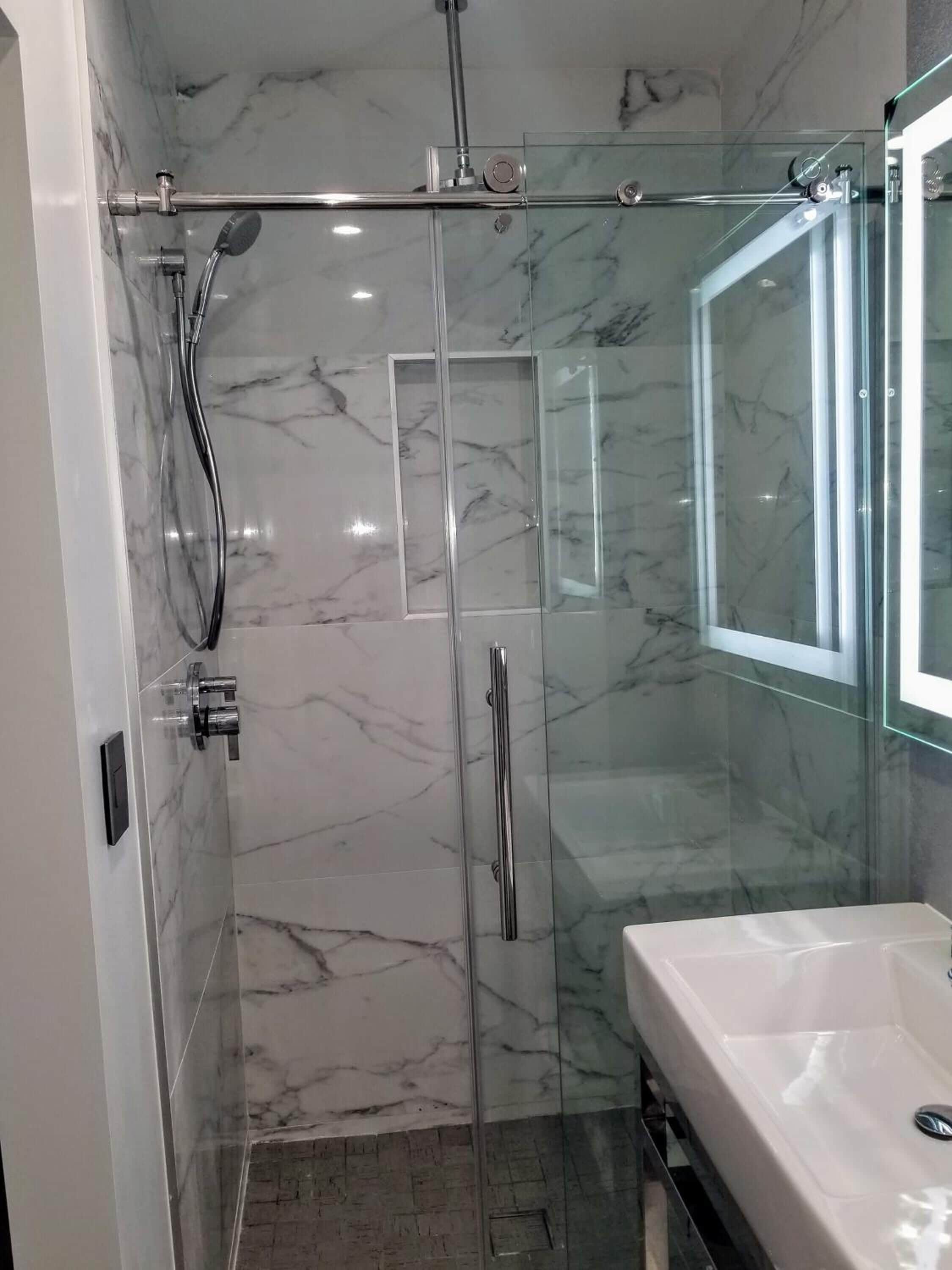 A modern bathroom with a glass-enclosed shower, marble walls, and a white sink.