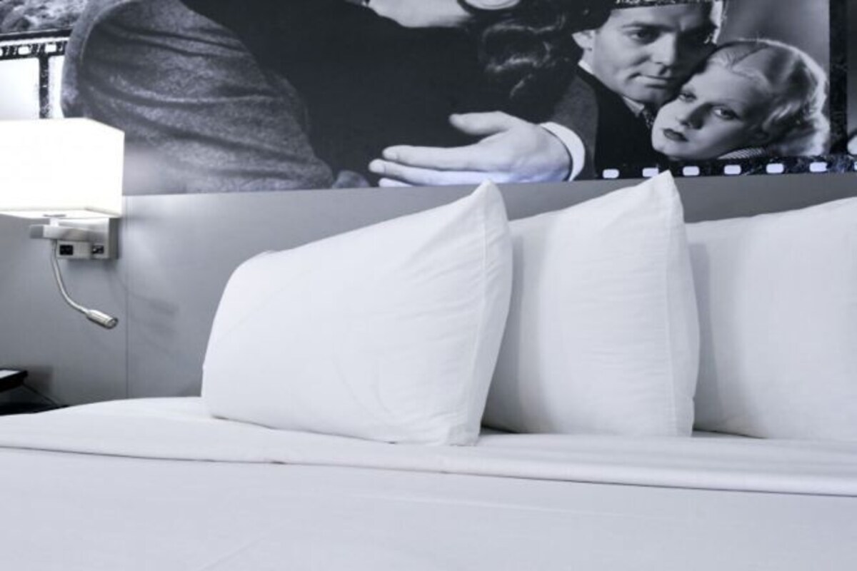 A bedroom with a bed, pillows, a nightstand, and a wall-mounted lamp.