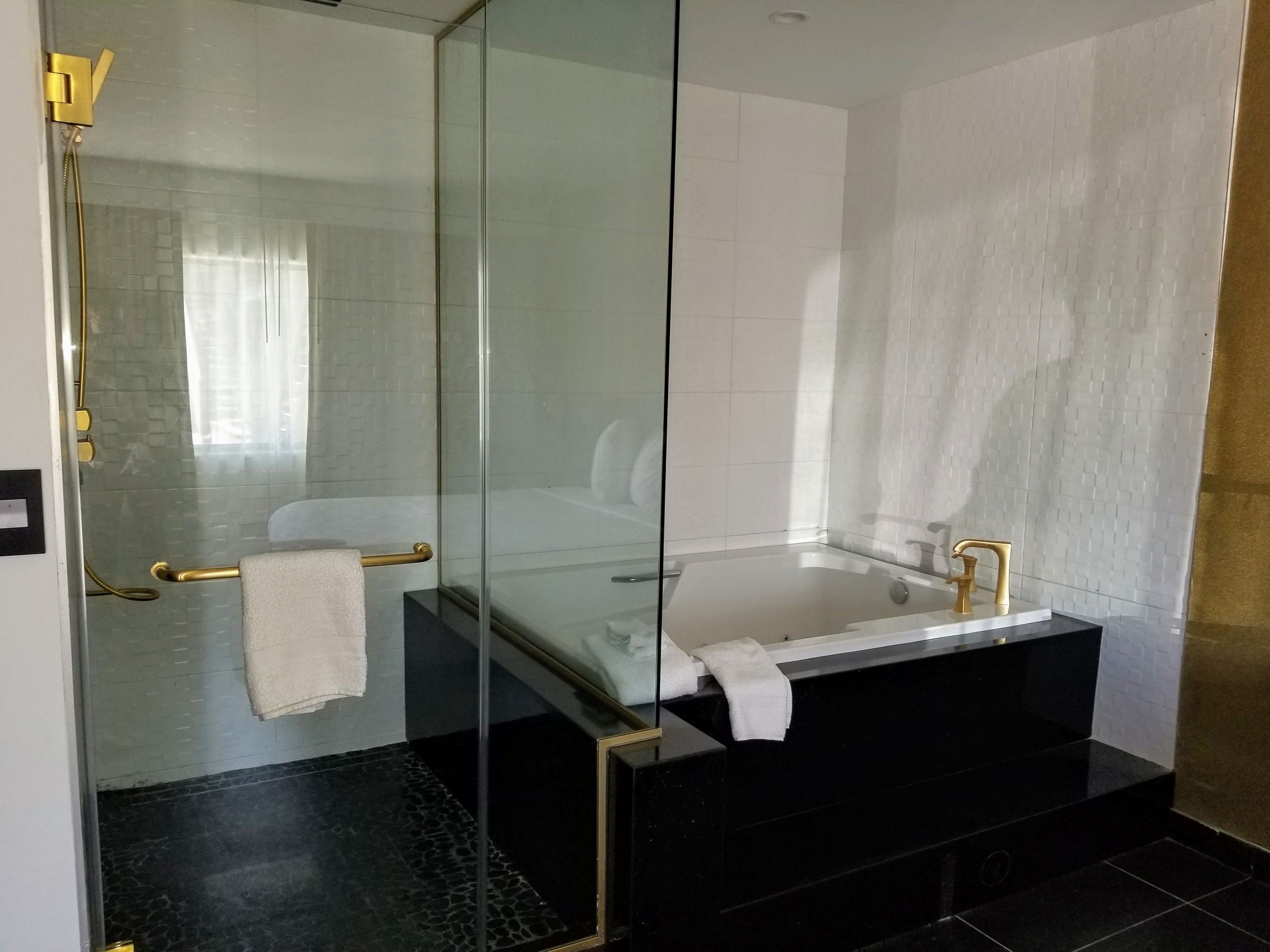Une salle de bain moderne avec une douche à l’italienne en verre, une baignoire noire et un mur recouvert de carreaux blancs.