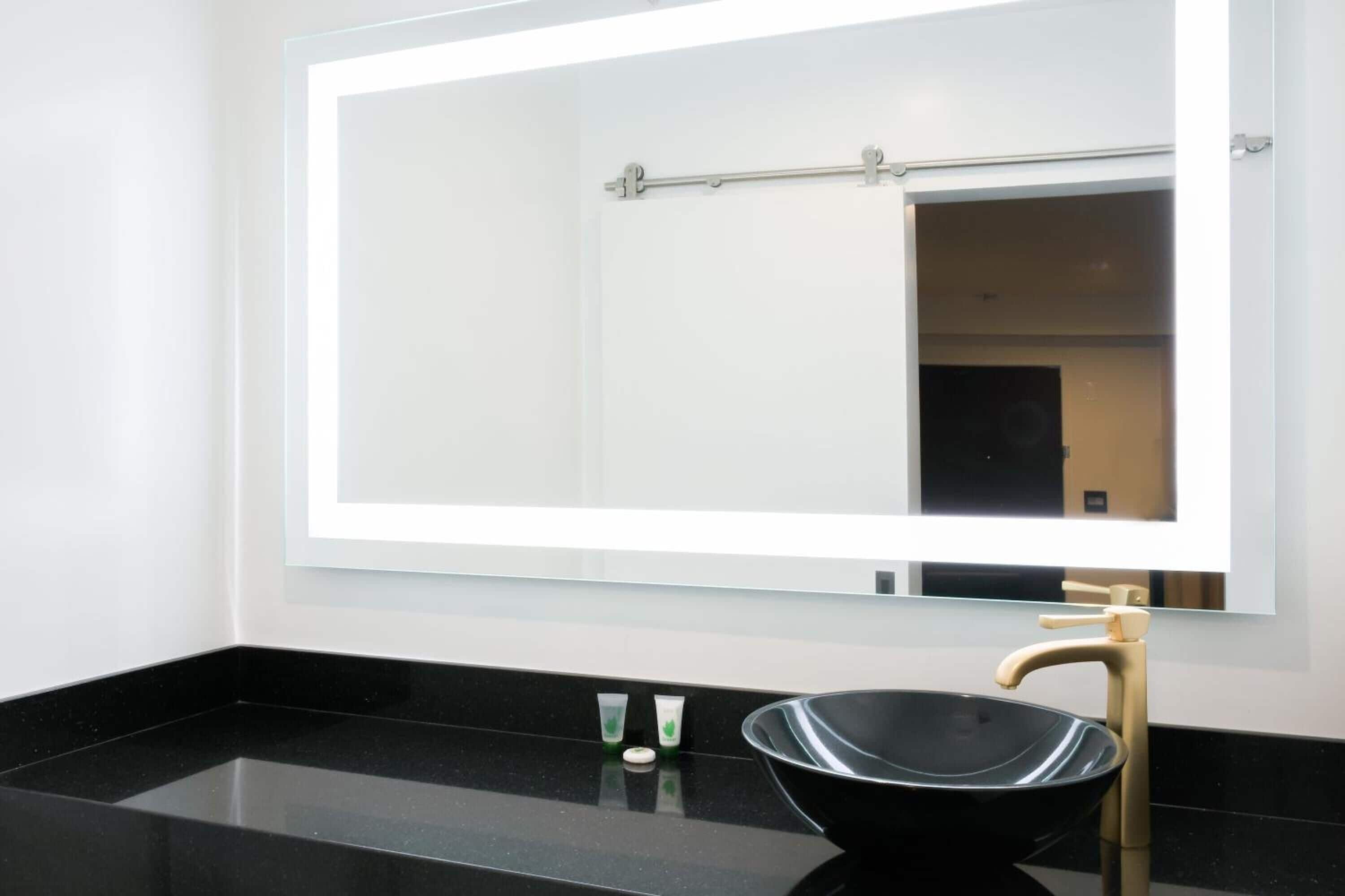 Ein modernes Badezimmer mit einem schwarzen Waschbecken, einem goldenen Wasserhahn und einem großen Spiegel mit Lichtleiste.