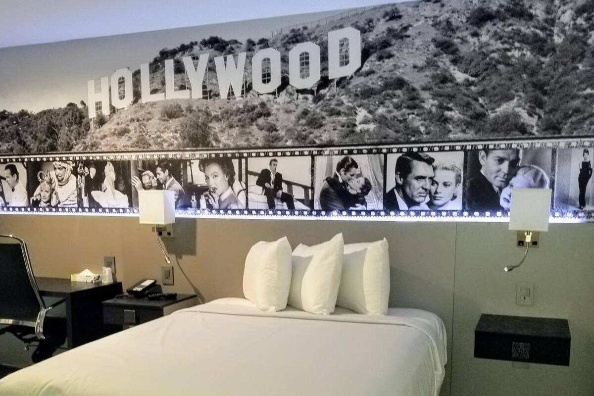 A hotel room with a large Hollywood-themed wall, a bed, a desk, and a chair.