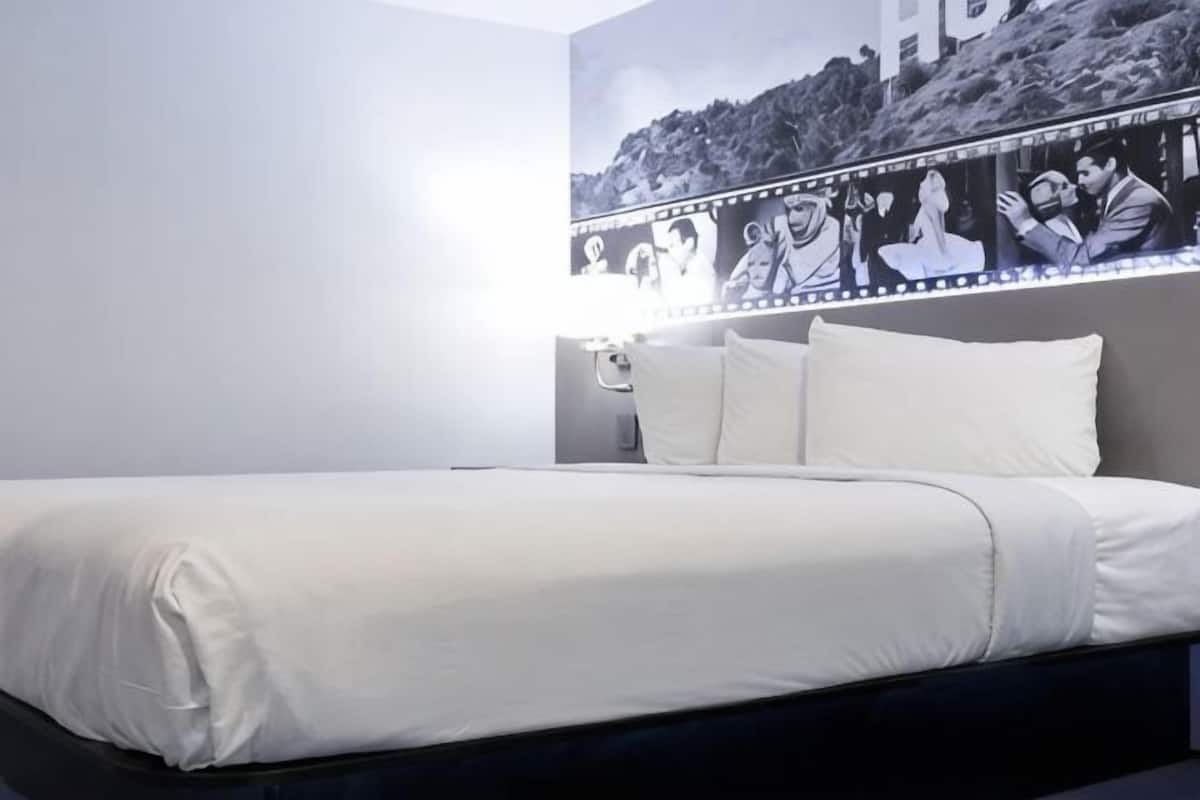 A bed with white bedding, a headboard with a mirror, and a wall with a black and white photo collage.