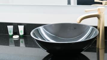 A black bowl sink with a gold faucet on a black countertop.