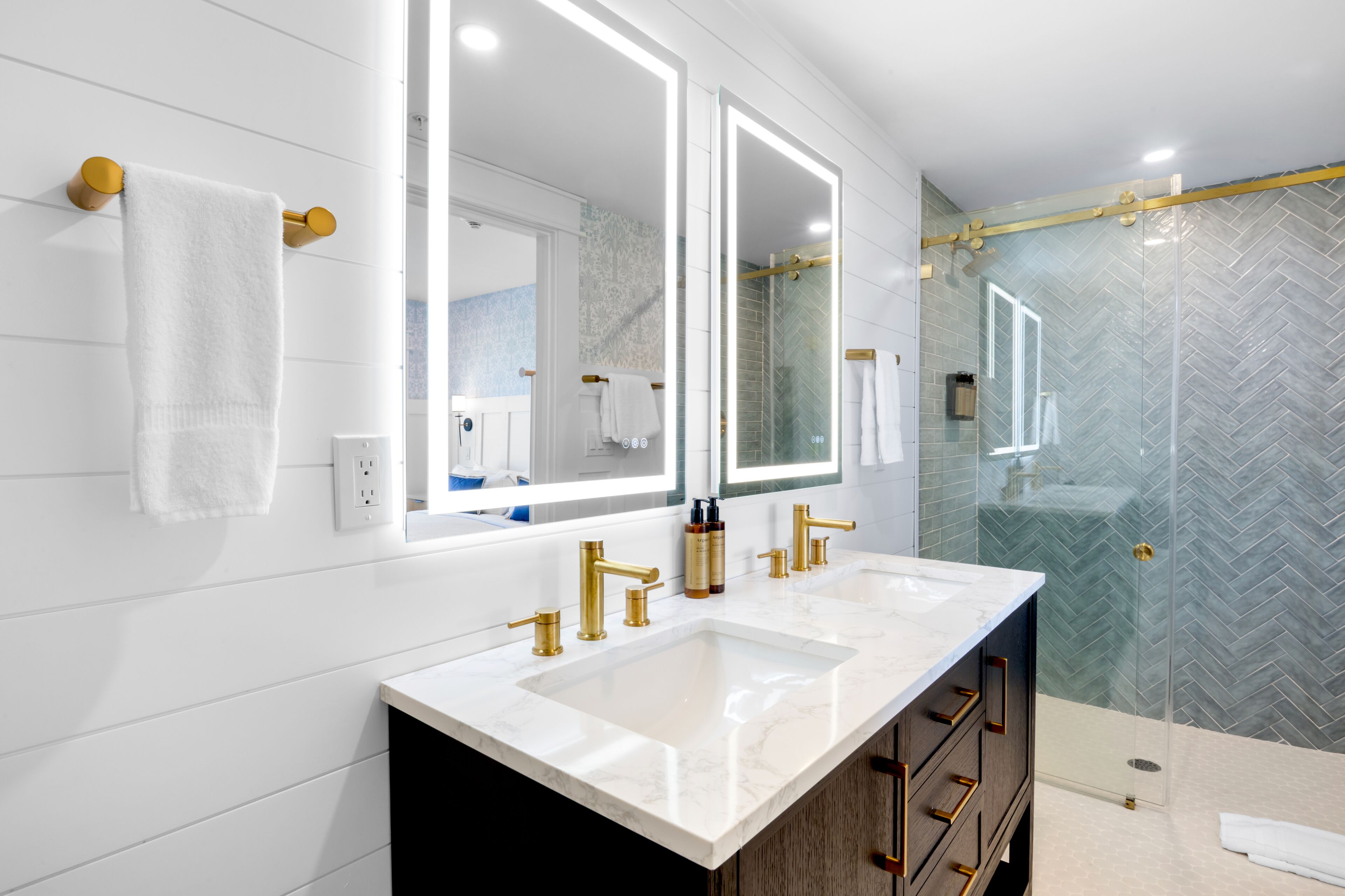 A modern bathroom with dual sinks, gold fixtures, and a glass shower enclosure.
