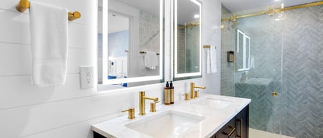 A modern bathroom with dual sinks, gold fixtures, and a glass shower enclosure.