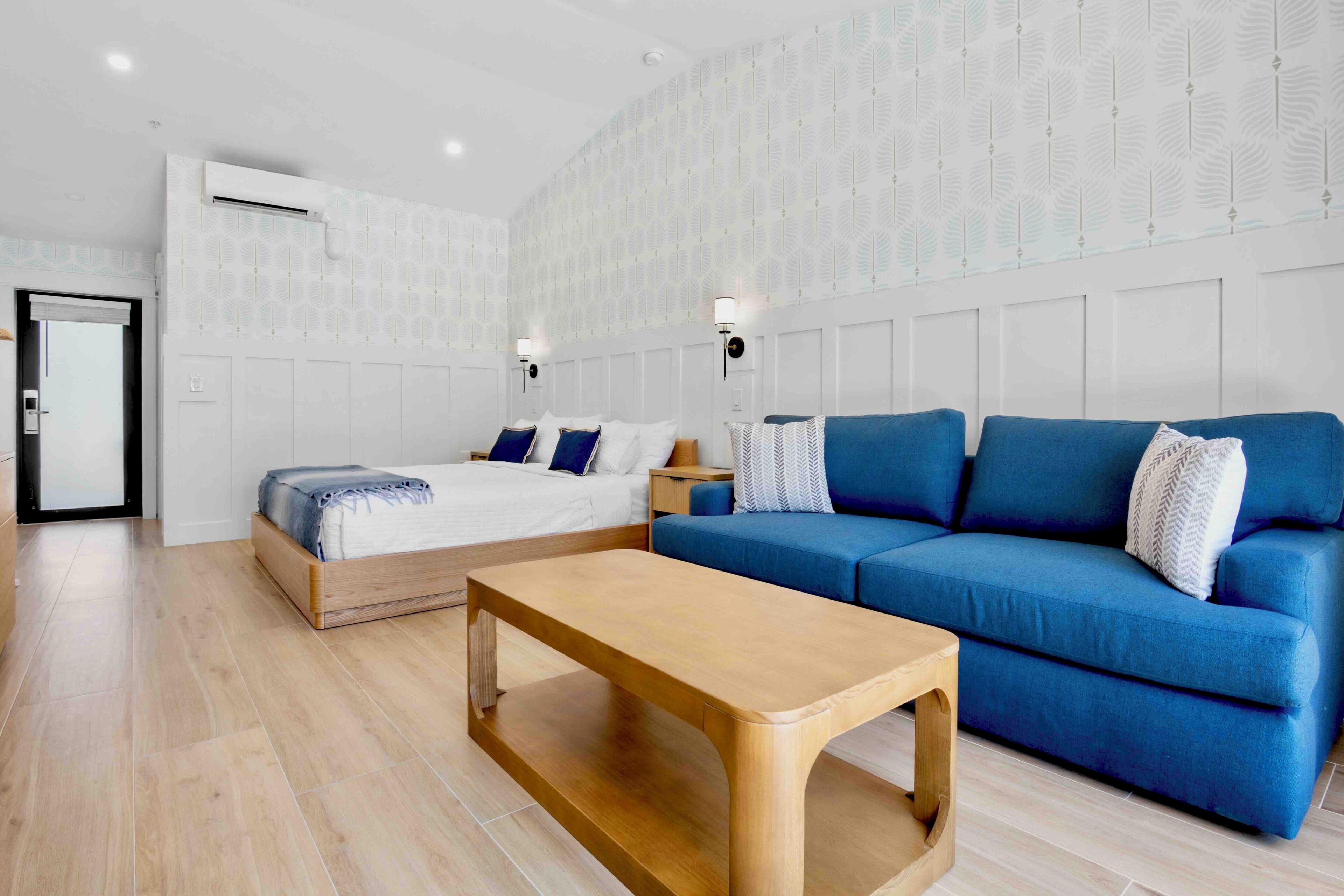Una habitación moderna con cama, sofá azul, mesa de centro de madera y papel tapiz estampado.