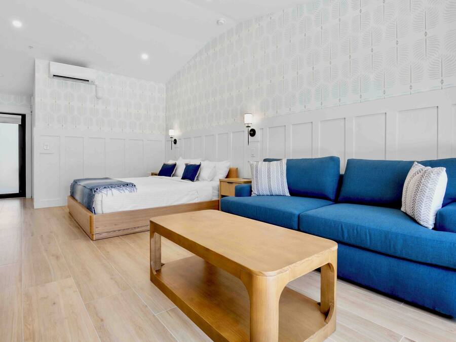 Una habitación moderna con cama, sofá azul, mesa de centro de madera y papel tapiz estampado.