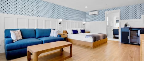 A modern room with a sofa, a bed, a wooden table, and a kitchenette area.
