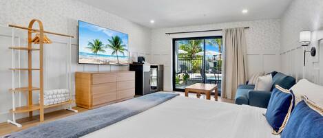 Un dormitorio con una cama grande, un escritorio, un armario, un televisor y un balcón con vistas a palmeras.