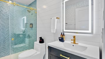 A modern bathroom with a glass shower enclosure, a white toilet, a vanity with a gold faucet, and a mirror with a door.