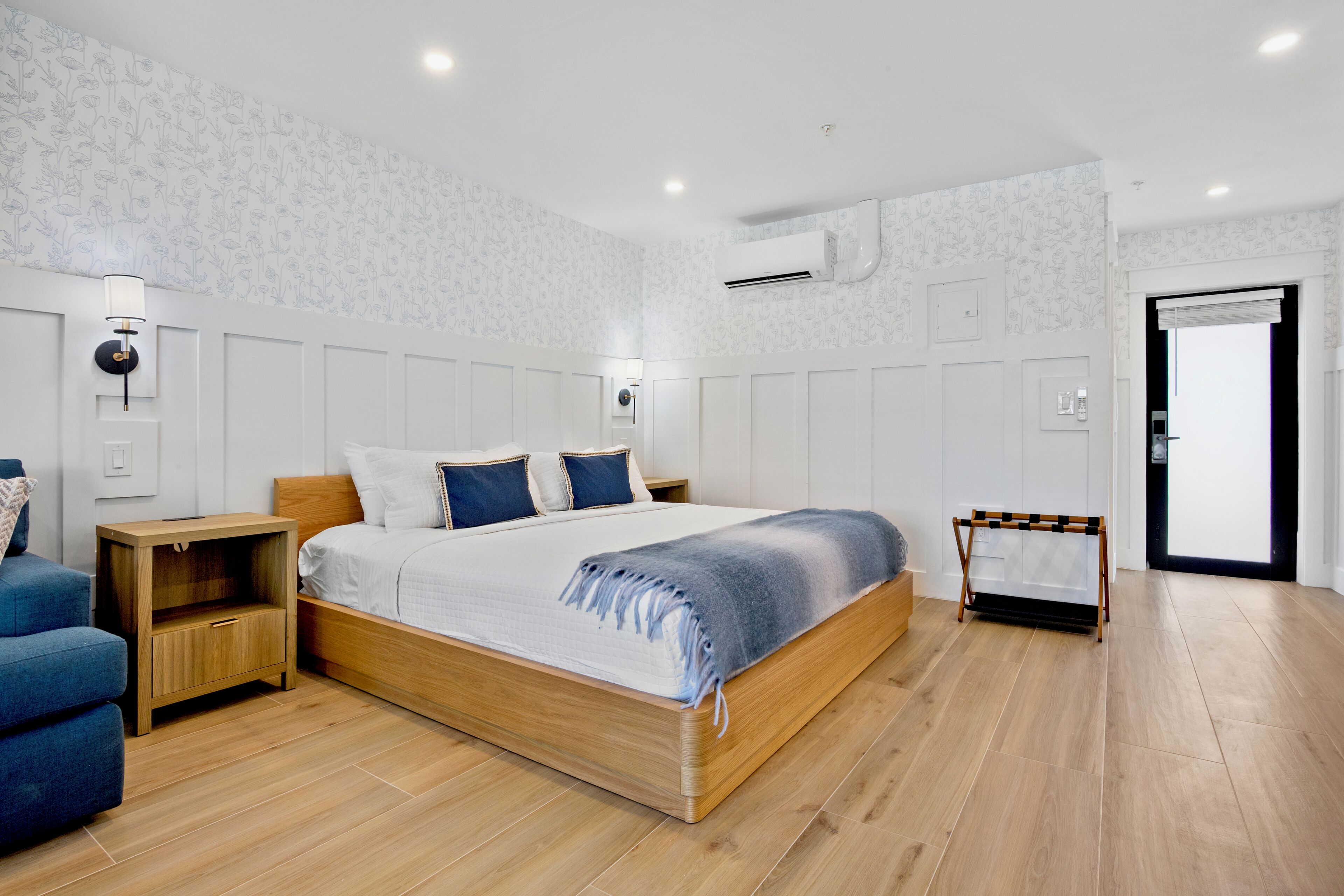 A bedroom with a wooden bed, a nightstand, a blue chair, and a wooden bench.