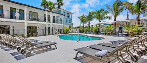A pool area with sun loungers and a building with balconies.