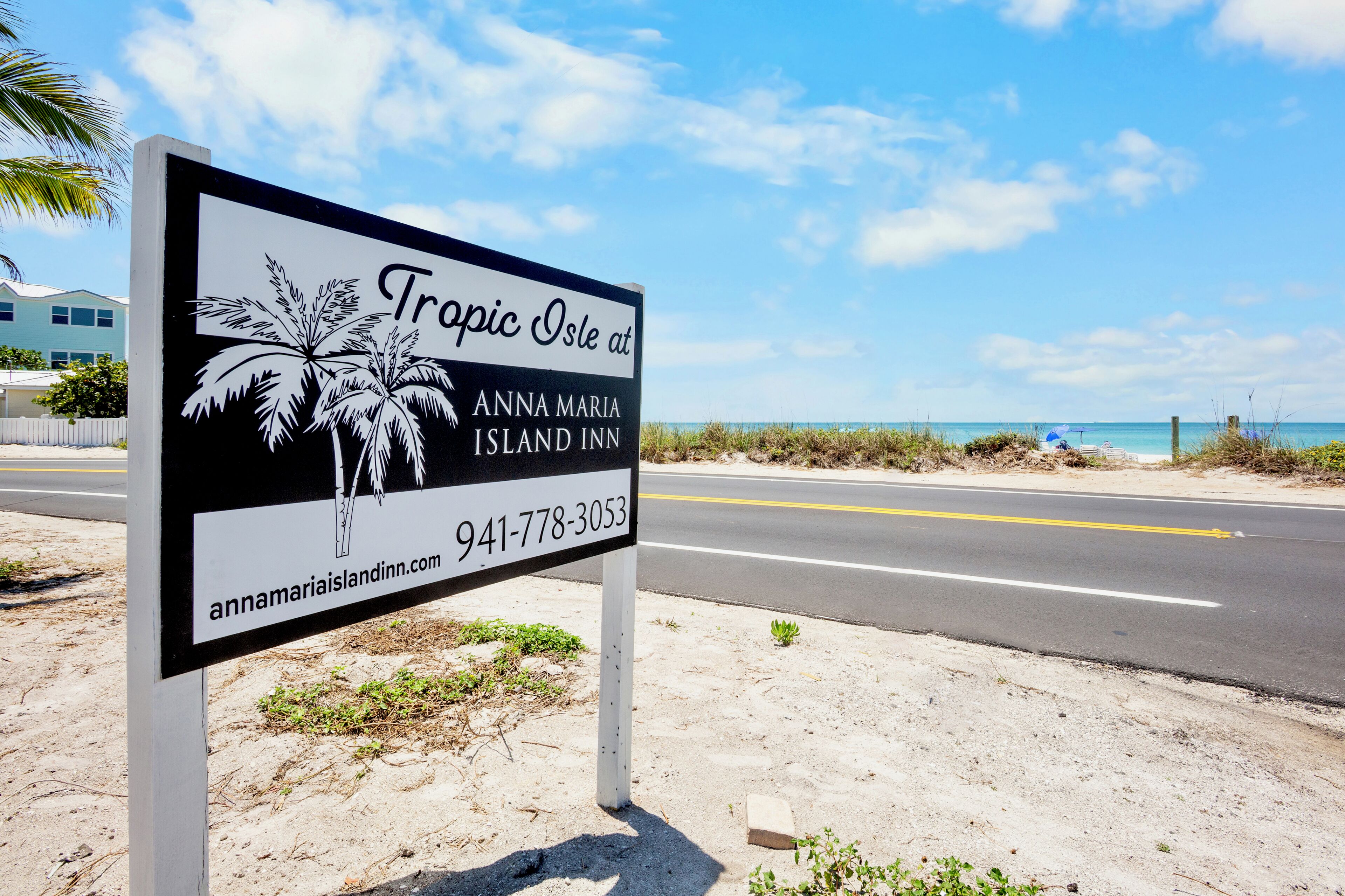 A sign for Anna Maria Island Inn with a palm tree graphic, contact number, and website URL.