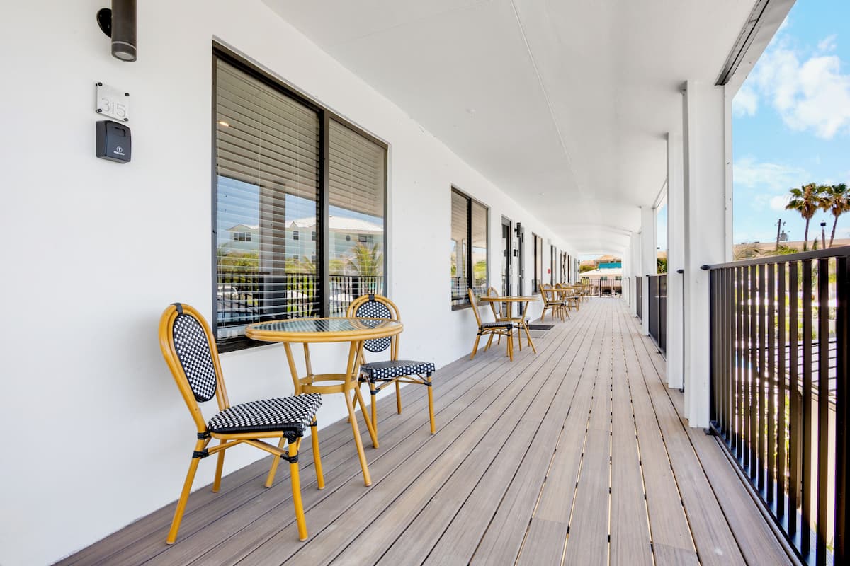 A covered outdoor area with wooden flooring, chairs, tables, and large windows.