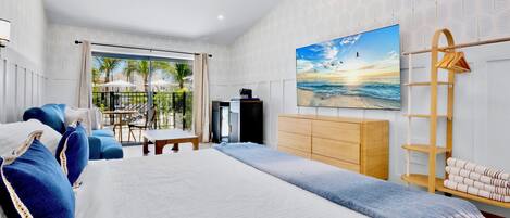 A modern hotel room with a large bed, a TV, a wooden dresser, and a balcony with outdoor furniture.